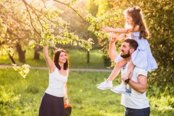 girl-sitting-her-fathers-shoulder-picking-tree-leaf-with-mother